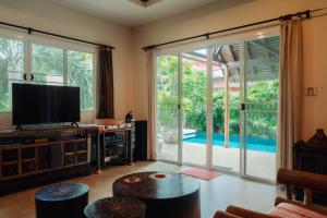 een woonkamer met een tv en een grote glazen schuifdeur bij Chaba Pool Villa in Nai Harn Beach
