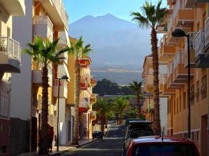 a street with palm trees and buildings with a mountain at Family and Friends , Familienapartment Playa de San Juan in Guía de Isora