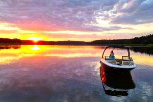 a man in a boat on a lake at sunset at Marina Glamour - 3pok, widok na jezioro, klimatyzacja, parking podziemny, winda, Netflix in Iława