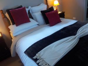 a large white bed with red and black pillows at Leafield Cottages in Dixons Creek