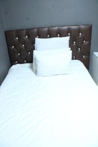 Cama blanca con cabecero marrón y almohadas blancas en Royal Guest House & and Lodge, en Pietermaritzburg