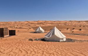 BadīyahPrivate Camel Safari Camp的沙漠中两顶白色帐篷,周围是一片沙地。
