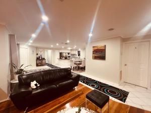 a living room with a black leather couch and a kitchen at Spacious 6 Bedroom Holiday Home 15 Min Away From Melbourne Airport in Sydenham