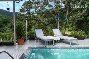 deux chaises et une table à côté d'une piscine dans l'établissement Stay Leisurely Pawna Lake Villa 3BHK, Pawna Lake, à Malavli