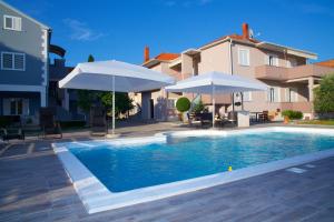 una piscina con 2 sombrillas y una casa en Antonija Apartments with Pool, en Biograd na Moru