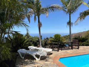 a pool with a table and chairs and palm trees at Villa feliz casa Los Abuelos B in Tijarafe