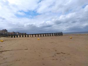 a sandy beach with a pier in the distance at Villa de l'epi Grandcamp Maisy in Grandcamp-Maisy