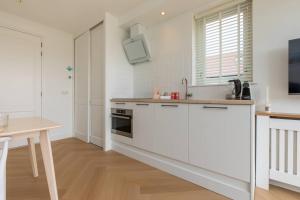 a white kitchen with a sink and a table at Hello Zeeland - Appartement Kusthuys 2 - 2025 in Zoutelande +15 photos