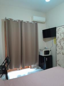 a bedroom with curtains and a bed and a microwave at Quarto suíte in Guaratuba