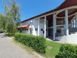a white building with a tree and bushes next to a sidewalk at Apartment in Zamardi - Balaton 53129 in Zamárdi