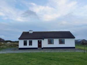 a white house with a red door in a field at Cottage 188 - Ballyconneely in Ballyconneely