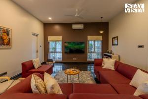 a living room with red couches and a tv at StayVista at The Lakeshore with Lake View, WiFi, Garden in Bengaluru