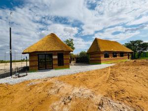 two buildings with straw roofs on a dirt field at Endambo Hides Lodge in Amakange