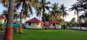 two small houses with palm trees in a yard at Stay Guru Resort Farm Villa in Bhuj