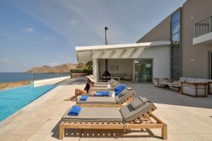 a woman is sitting on a poolside bed next to a house at Thalassa Residence, Heated Pool, Hot Tub & SeaView in Panormos Rethymno