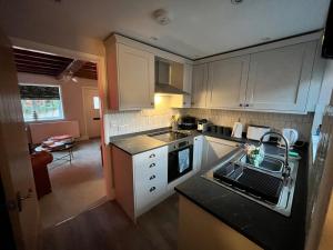 a kitchen with white cabinets and a black counter top at Boutique style cosy cottage in Ellesmere