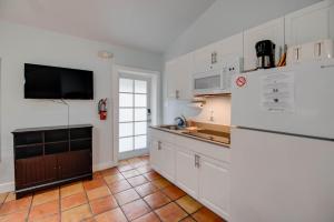 a kitchen with white cabinets and a tv on the wall at Ibis Suite - Southernmost Sanctuary in Key West