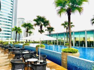 una piscina de hotel con mesas, sillas y palmeras en KLCC Vortex Suites Residence, en Kuala Lumpur