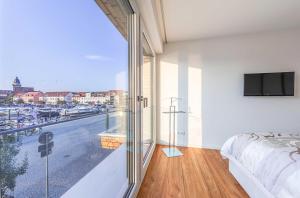 a bedroom with a balcony with a bed and a television at Hafenblick - Wohnung in der Hafenresidenz mit Balkon & Wasserblick in Waren