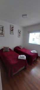 Habitación con 2 camas con sábanas rojas y ventana en Kattegat, en Puerto Madryn 3 fotos más