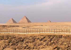 a view of pyramids in the desert with a fence at Pyramids Panorama Suites in ‘Ezbet `Abd el-Ḥamîd