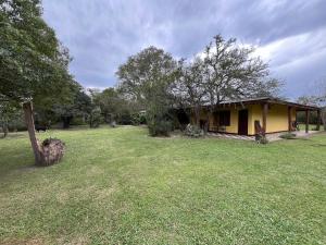 a small yellow house in a field with trees at Posada el Yacaré in Colonia Carlos Pellegrini