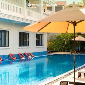 a swimming pool with an umbrella next to a building at Wyndham Garden Hoi An Cua Dai Beach in Hoi An