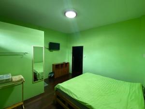 a green bedroom with a bed and a mirror at Baanmakpoo บ้านหมากพลู in Sangkhla Buri