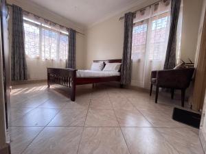 a room with a bed and a chair and windows at Royal Bukoto Villas in Kampala