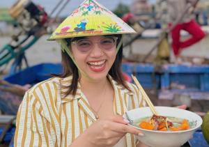 a woman wearing a party hat holding a bowl of food at Fabulous Mekong Homestay in Can Tho +9 photos