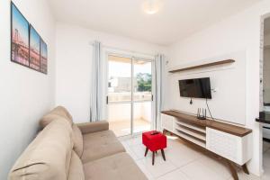 a living room with a couch and a tv and a red stool at Apartamento moderno na Pedra Branca in Palhoça