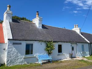 a blue bench sitting outside of a white house at Ceol-na-Mara in Berriedale