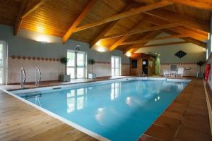 a large swimming pool in a large room with wooden ceilings at Ash Cottage - Escape to Pembrokeshire Cottage with Pool & Sauna in HAW
