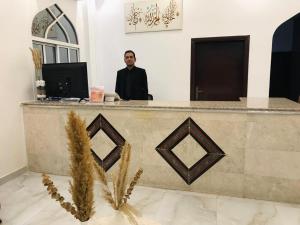 a man standing behind a counter in a room at Taj Al Arab Hotel Al Burimi in Al Buraymī