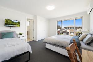 a white bedroom with two beds and a window at KozyGuru | Austral | Convenient 4 x Ensuite House in Austral