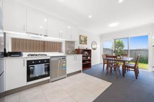 a kitchen with white cabinets and a table with chairs at KozyGuru | Austral | Convenient 4 x Ensuite House in Austral