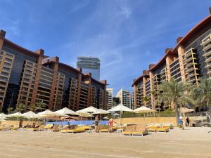 a beach with chairs and umbrellas in front of buildings at Emerald at Tiara Beach Residences with Atlantis views in Dubai