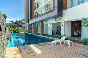 a building with a swimming pool and two white chairs at Chic Condo in Karon by Lofty in Karon Beach