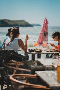 two women sitting at a table on the beach with wine glasses at Polzeath Beach House in Polzeath