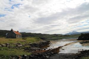 a house in a field next to a river at Cragaig Bothy in Geasgill Mòr