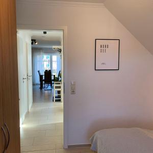 een slaapkamer met een witte muur met een schilderij aan de muur bij Haus-am-See-Kolkstr-1-OG-rechts in Norddeich +7 foto's