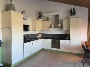 a kitchen with white cabinets and a clock on the wall at De Paer - Hof van Libeek in Sint Geertruid