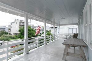 a porch with a wooden bench and an american flag at Craft Upper Unit by Bryant Real Estate in Wrightsville Beach