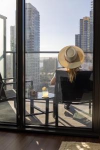 une femme dans un chapeau assise dans une chaise et regardant par la fenêtre dans l'établissement Kasa Little Italy San Diego, à San Diego
