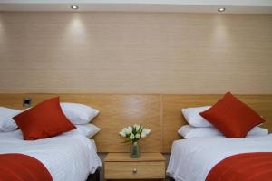 two beds with red and white pillows and a vase of flowers at Hill Park Hotel in Rosyth