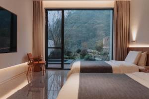 two beds in a hotel room with a large window at 峨眉山和院一溪清音酒店 in Emeishan City