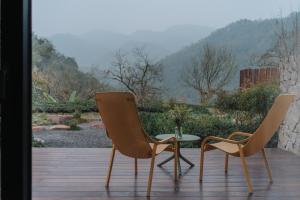 two chairs and a table on a wooden deck at 峨眉山和院一溪清音酒店 in Emeishan City