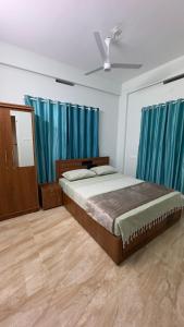 a bedroom with a large bed with blue curtains at The Karlyle Homestay in Vaduvanchal