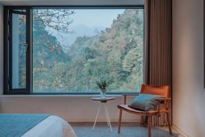 a bedroom with a large window with a chair and a table at 峨眉山和院一溪清音酒店 in Emeishan City