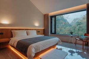 a bedroom with a large bed and a large window at 峨眉山和院一溪清音酒店 in Emeishan City